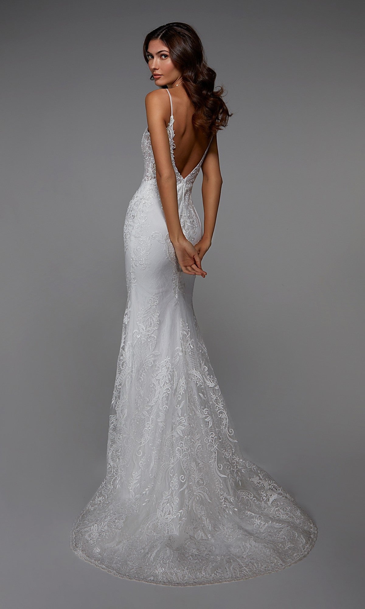 A woman models the Long White Dress: Alyce 7028—a fitted, backless white lace gown with delicate embroidery, thin straps, and a flowing train—against a gray background. Ideal for formal events or wedding inspiration.